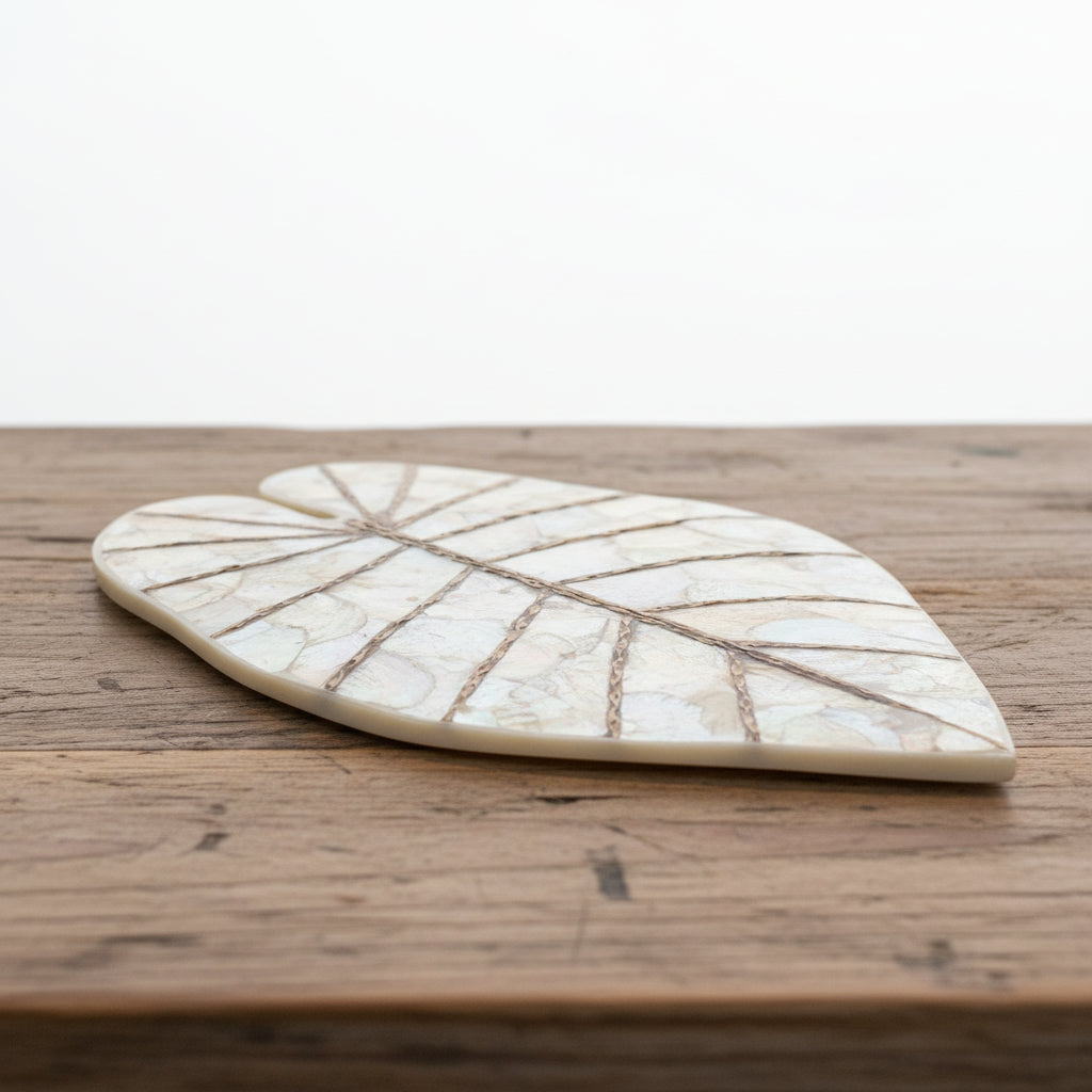 A heart-shaped leaf-shaped wall plaque made of iridescent mother-of-pearl with twine detailing, mounted on a carved wooden panel.