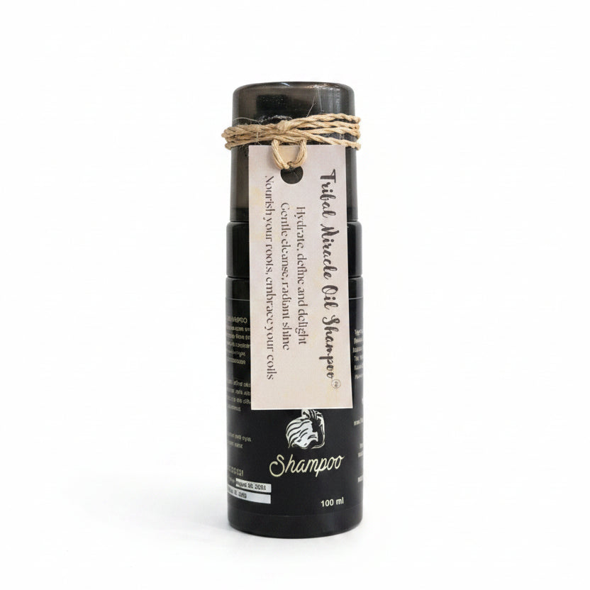A black bottle of Tuiled Miracle Oil Shampoo with a white paper label and a rustic jute twine bow, displayed on a white textured cloth in a shop setting.